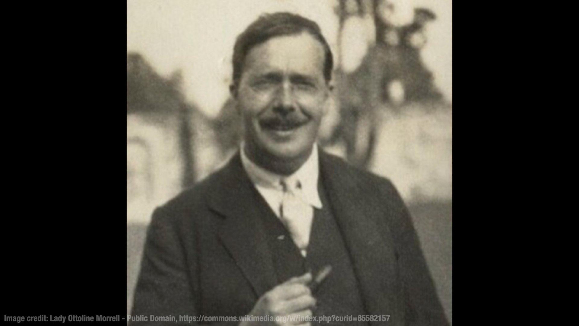 A grainy black-and-white picture of LP Hartley. He’s standing outside, smiling genially at the camera, and holding a pipe.
