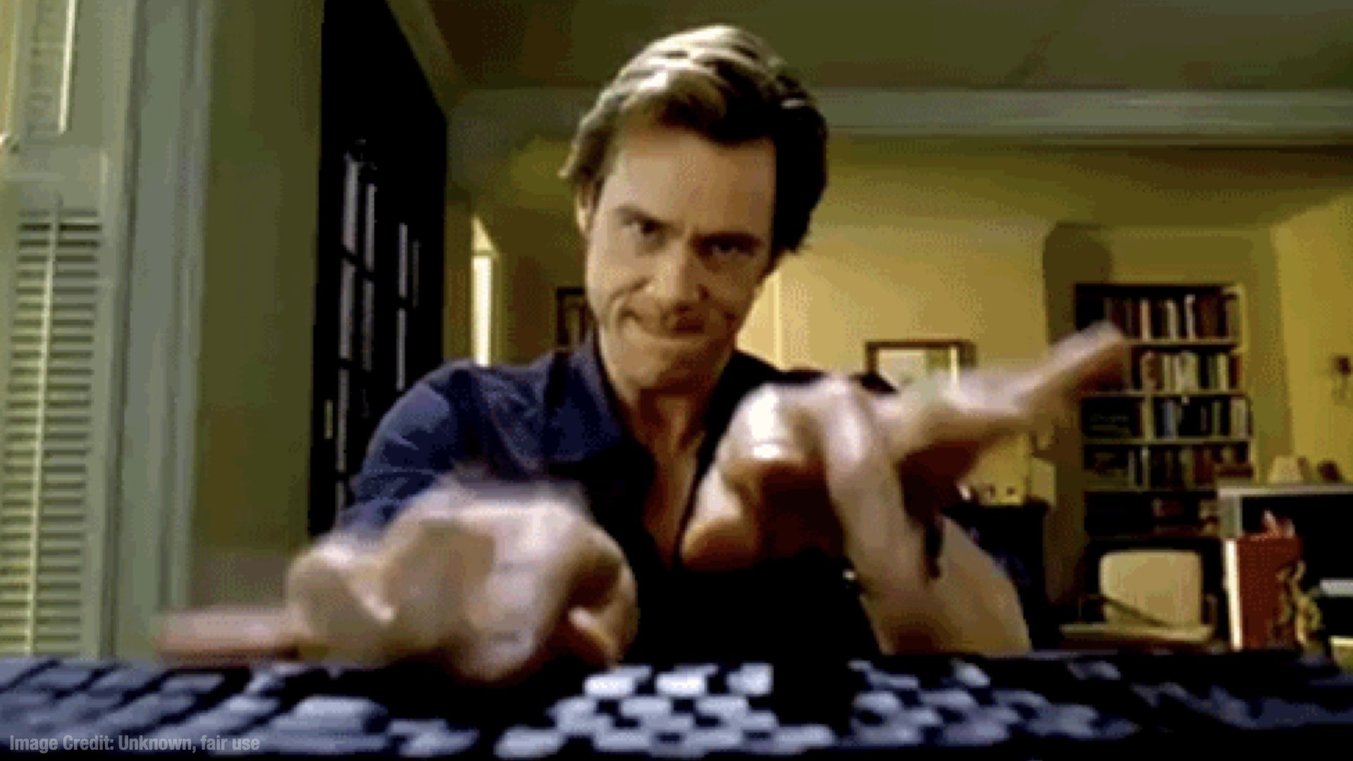 A dramatic cinematic shot of a man typing frantically at a keyboard as he stares into the camera.